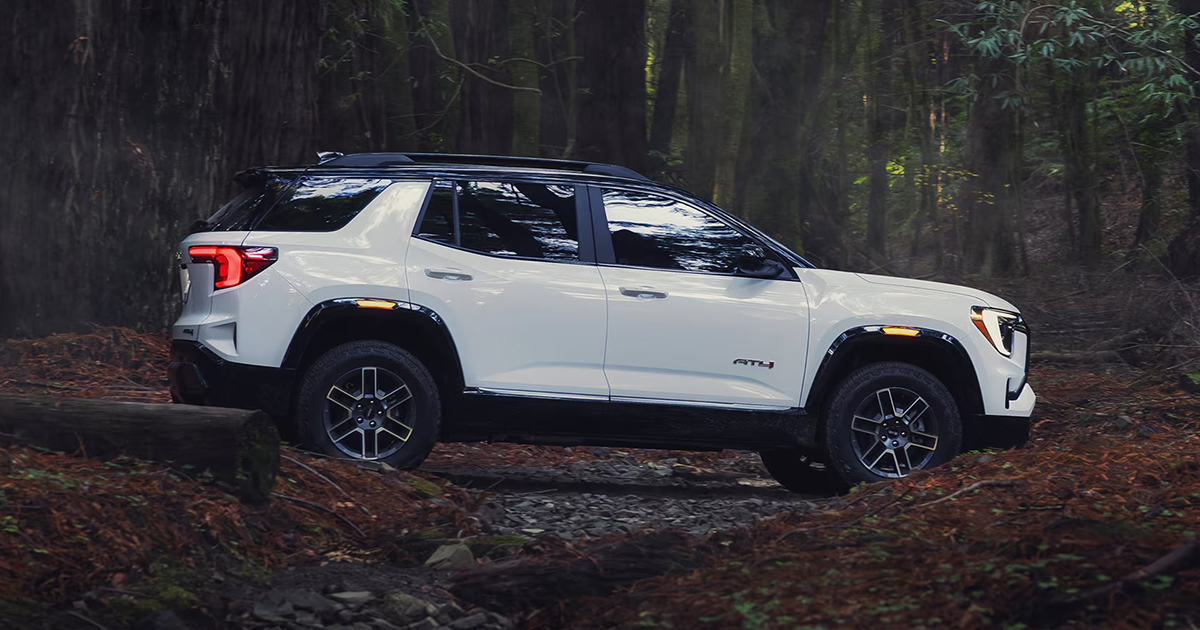 White 2026 GMC Terrain AT4 side profile view in wooded setting highlighting ground clearance and rugged design