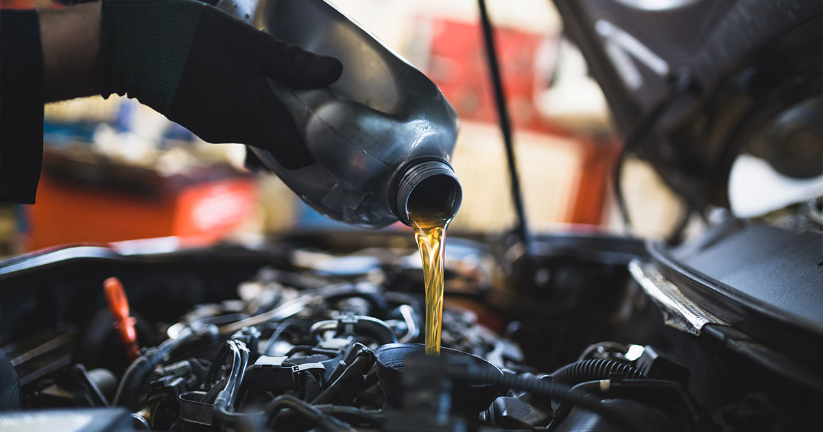 Professional automotive technician pouring engine oil during routine vehicle maintenance service