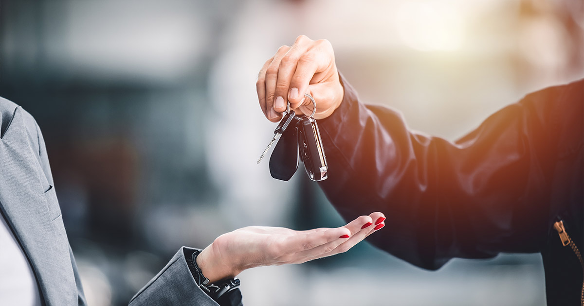 Car dealership staff member handing over vehicle keys to customer during car purchase or trade-in transaction