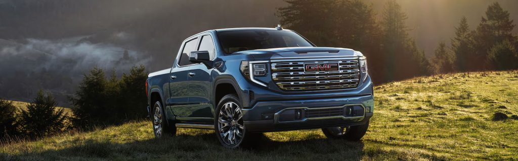 Blue GMC Sierra 1500 pickup truck parked in a scenic mountain landscape, showcasing its bold grille and rugged capability.