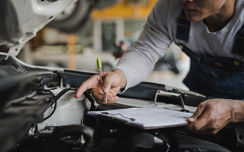 Automotive technician inspecting a vehicle engine and completing a maintenance checklist during a professional service appointment.
